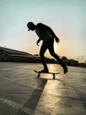 Sunset silhouette of a skater pushing along a riverfront promenade on a sleek board