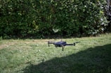 A drone hovers above a grassy lawn with a dense green hedge in the background.
