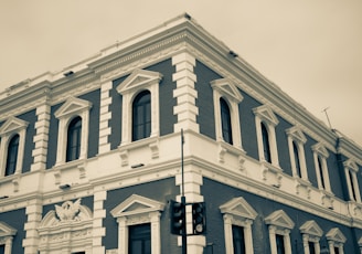 A historic, multi-story building displaying classic architectural details with white and dark brick accents. The facade features ornate window frames and decorative elements, with modern streetlights visible in the foreground.