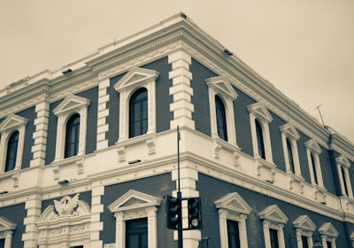 A historic, multi-story building displaying classic architectural details with white and dark brick accents. The facade features ornate window frames and decorative elements, with modern streetlights visible in the foreground.