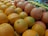A vibrant assortment of citrus fruits includes oranges and grapefruits, piled together with individual fruit stickers visible. The background shows additional piles of lemons, limes, and apples.