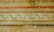 An ornate, vintage-looking wall mural featuring horizontal stripes in warm earth tones, including browns, reds, and golds. Interspersed among these stripes are intricate vine patterns with green leaves and winding ribbons, giving a classical and aged appearance.