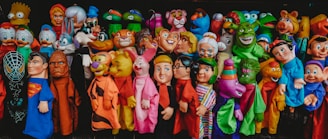 A colorful assortment of character-themed puppets displayed in a vibrant array. Each puppet represents a distinct fictional character, featuring exaggerated facial features, diverse colors, and whimsical expressions, all lined up closely together.