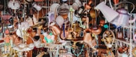 A chaotic array of assorted vintage and rustic metal objects hanging and displayed in an eclectic manner. The collection includes kettles, lamps, chains, and various other metallic containers, creating an antique and cluttered aesthetic.