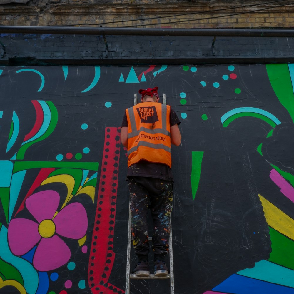 man standing on ladder leaning on wall with mural