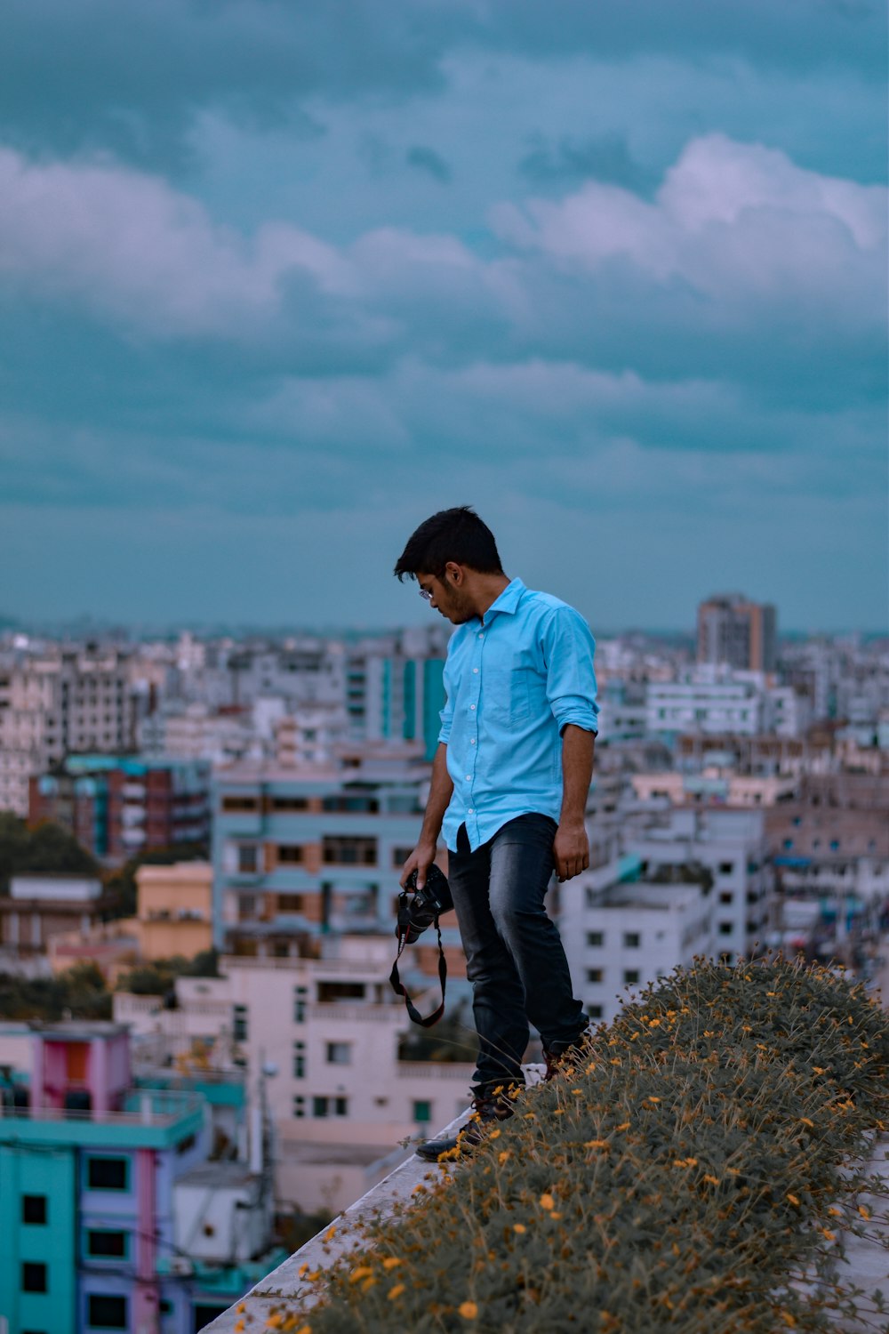 man standing on ledge looking down at the city beside flowers