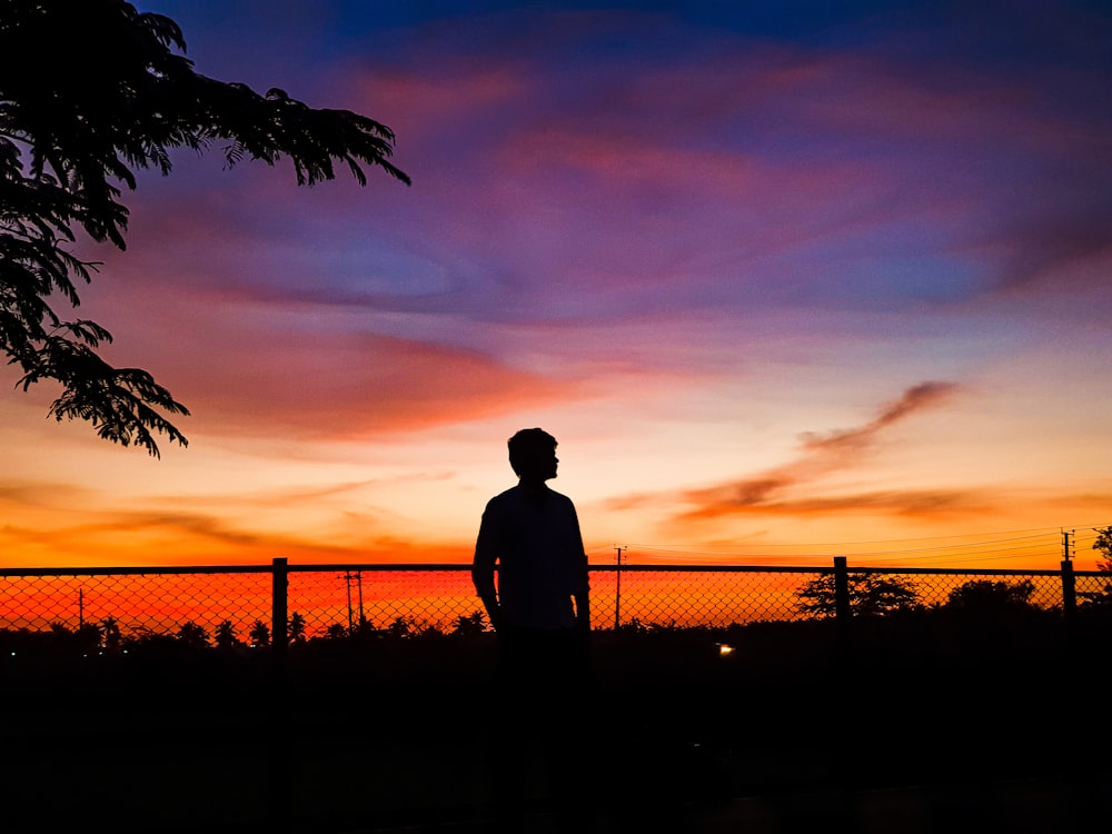 man standing in front of chain link fence during golden hour