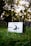 A small amplifier with a front panel featuring a large knob and headphone jack is placed on the grass. The brand name 'Erzetich' is visible on the device. The background is composed of blurred trees and foliage, suggesting an outdoor setting.