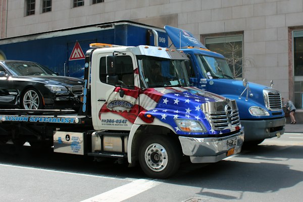 Patriotic-livery tow truck loading a black BMW on a city street