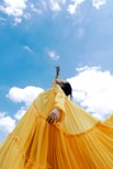 woman wearing yellow long-sleeved dress under white clouds and blue sky during daytime
