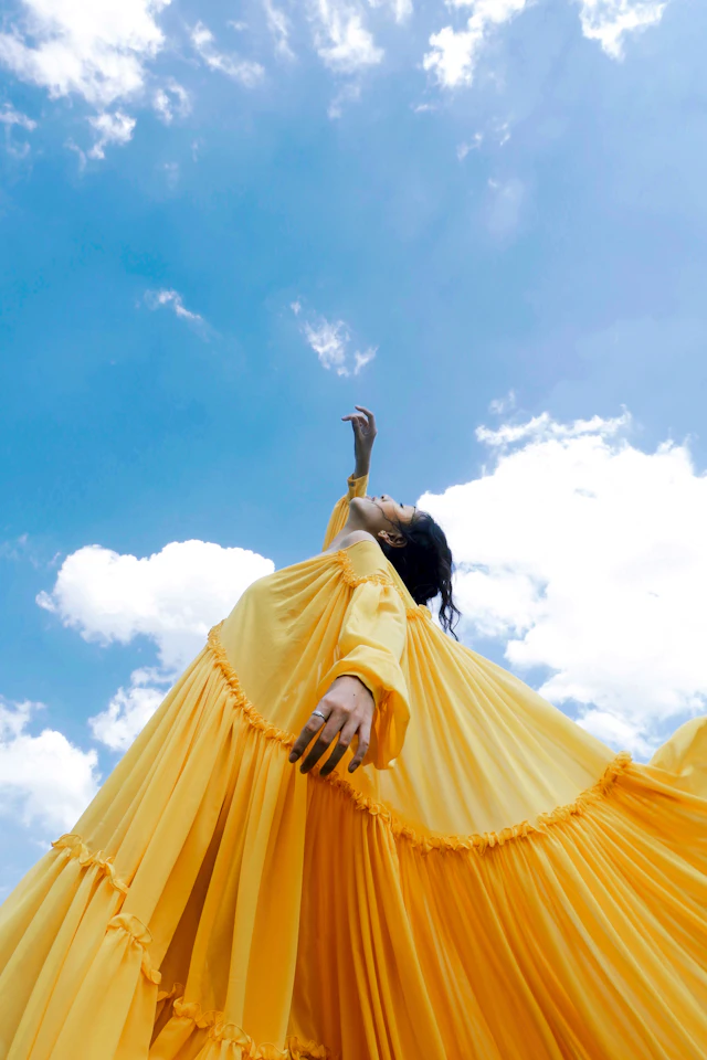 Woman in a yellow dress photographed against clouded daylight