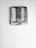 A square wall clock with a silver frame is mounted on a textured white wall with visible cracks. The clock has a minimalist design with thin black hands and simple hour markers.