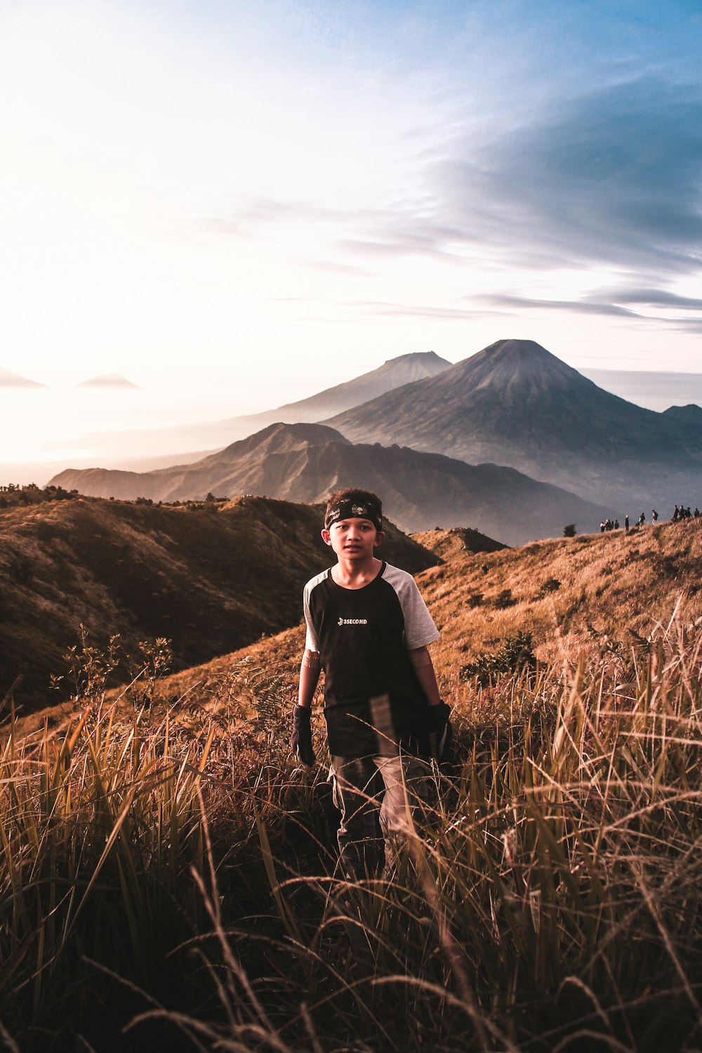 man standing between grasses facing mountains