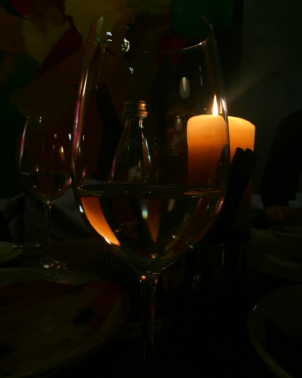 Weißwein im Weinglas neben angezündeten gelben Stumpenkerzen