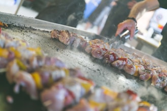 Close-up of a sizzling grill with skewers of meat and vegetables being cooked.