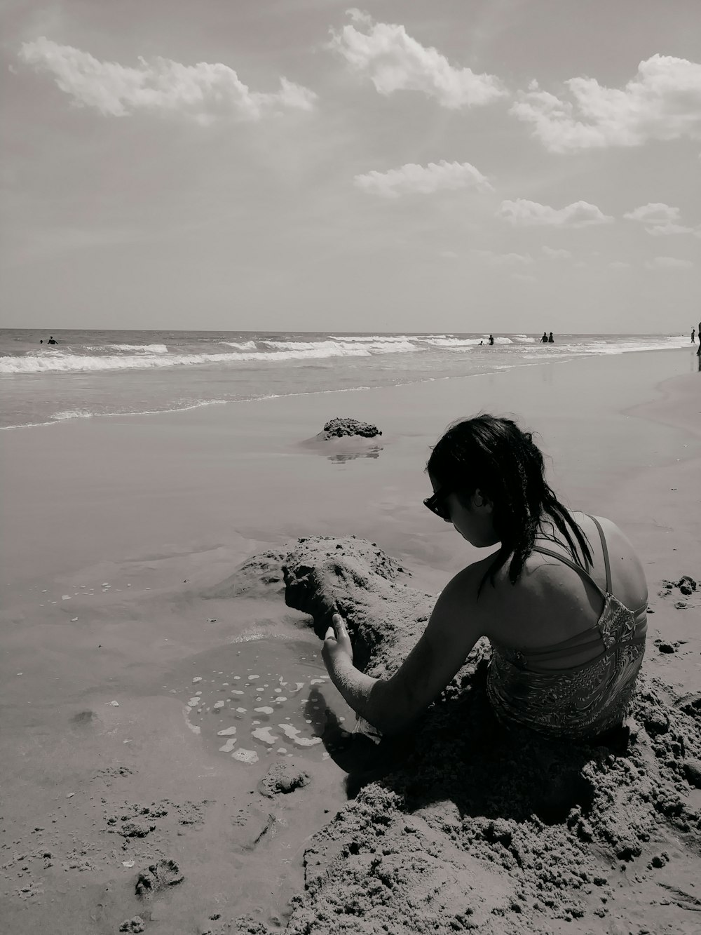 해변에 앉아있는 여자의 회색조 사진