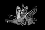 A cluster of clear, angular crystals arranged in a complex formation with sharp edges and varying sizes, set against a black background.