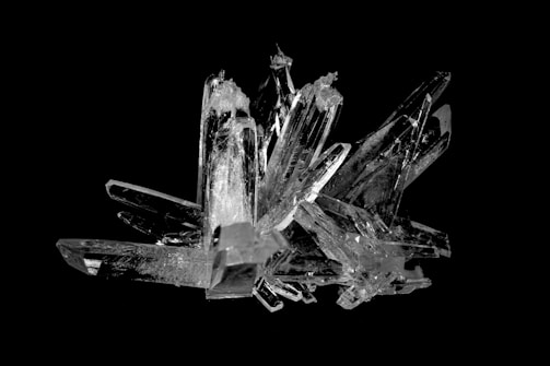A cluster of clear, angular crystals arranged in a complex formation with sharp edges and varying sizes, set against a black background.