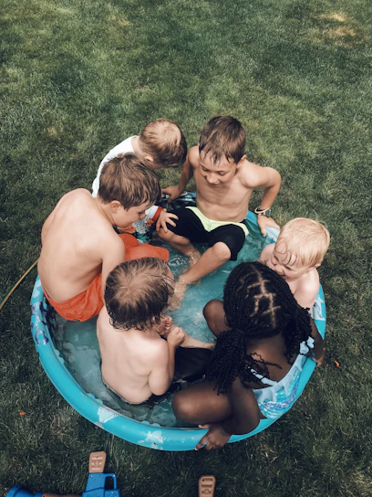 A group of children and instructors smiling during a swimming lesson at a sunny community pool.