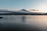 A scenic shot of Mount Fuji reflected in a calm lake during sunrise.
