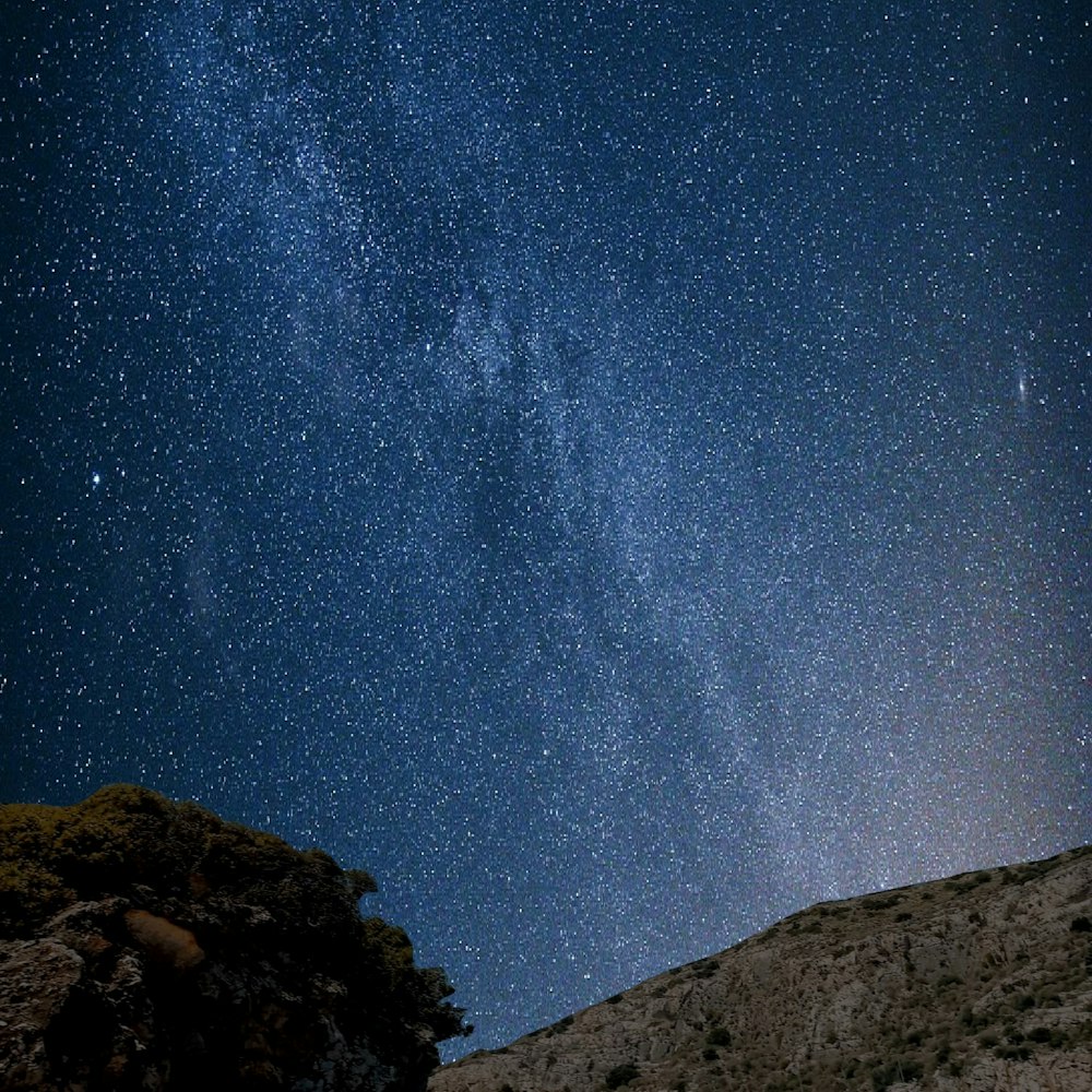 the night sky is filled with stars above a rocky hill