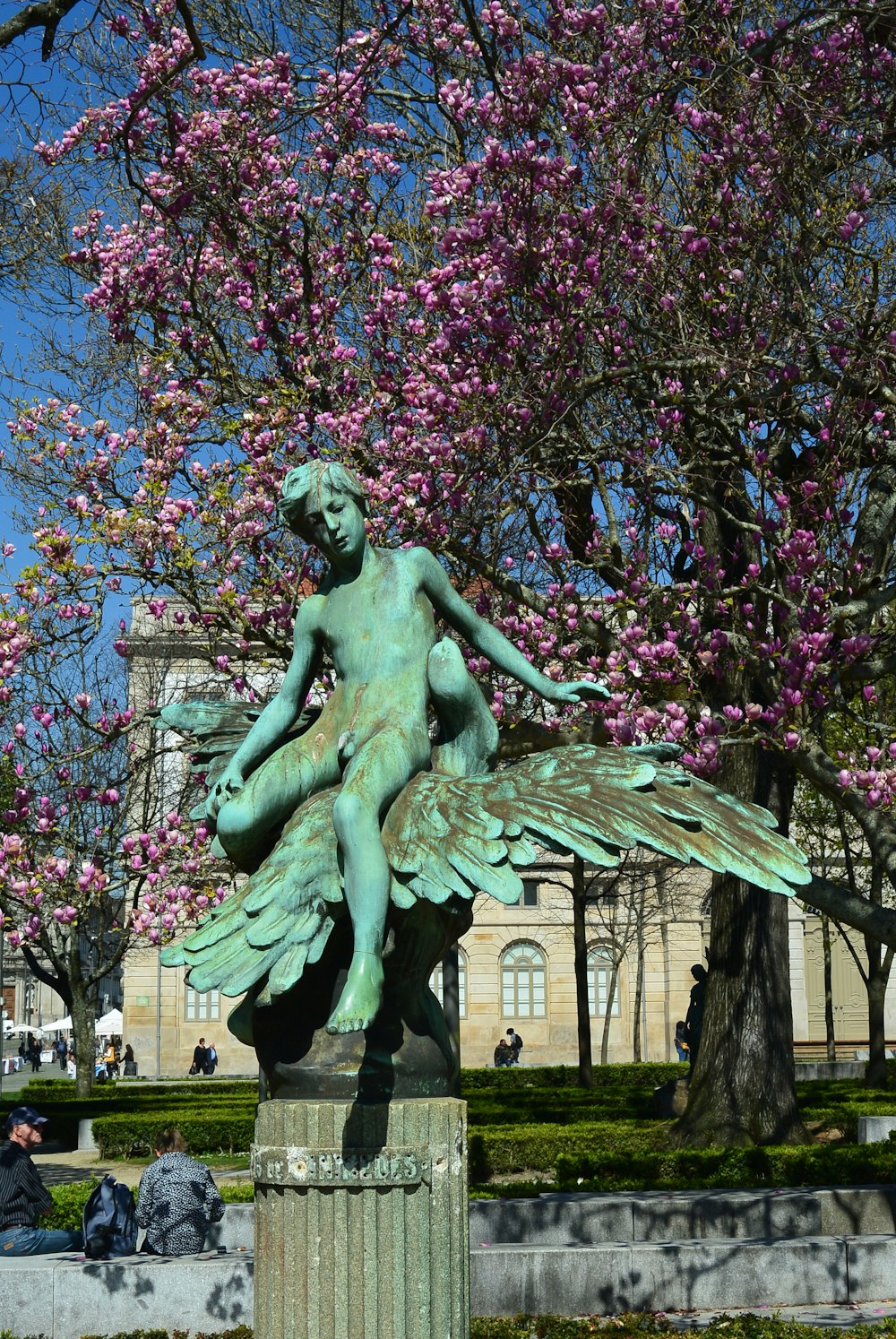 nude angel sitting statue near flowering tree