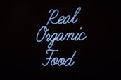 Neon sign displaying the words 'Real Organic Food' in a flowing script against a dark background.