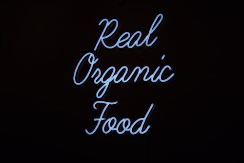 Neon sign displaying the words 'Real Organic Food' in a flowing script against a dark background.