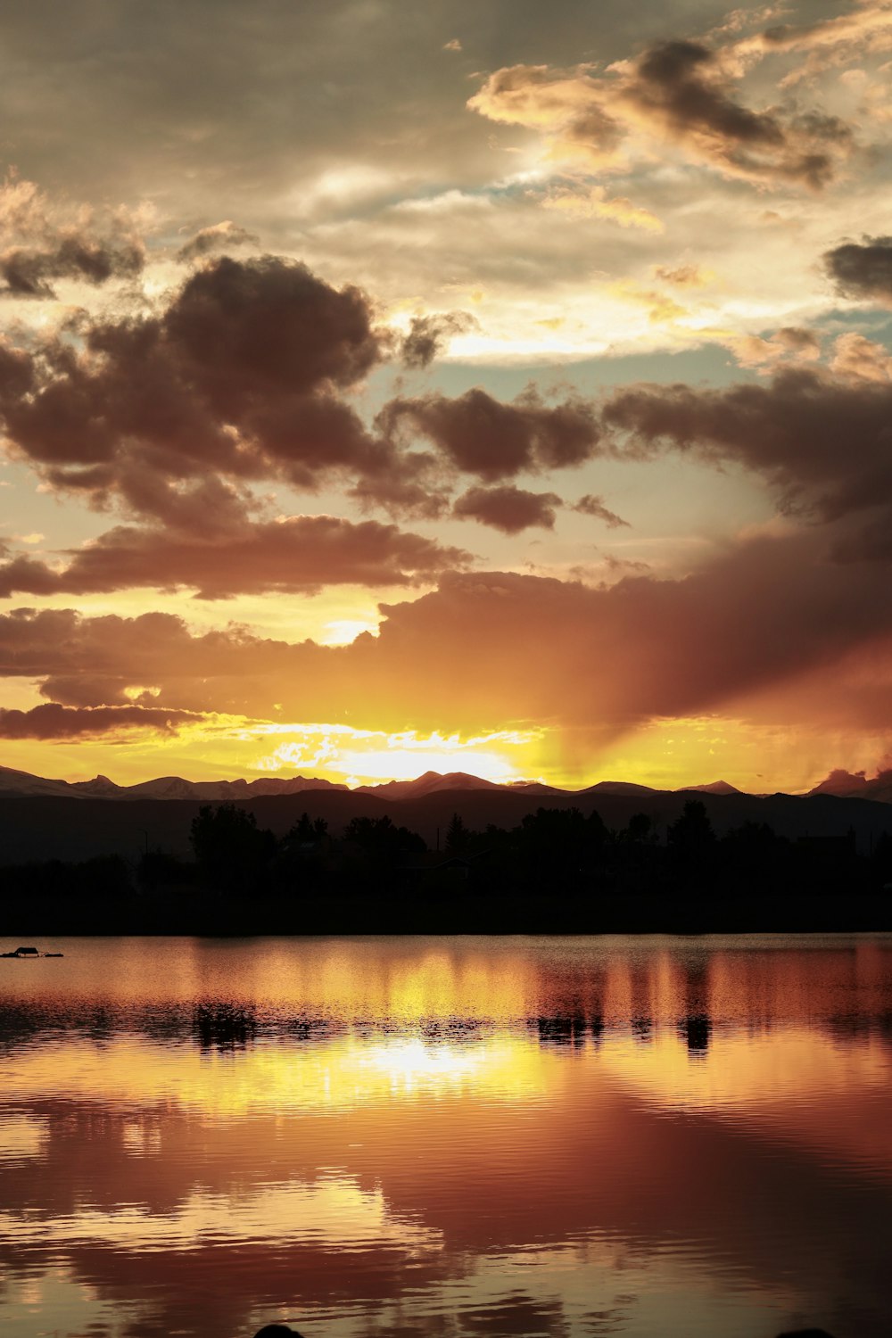 silhouette of mountain and trees near lake under orange sky and clouds