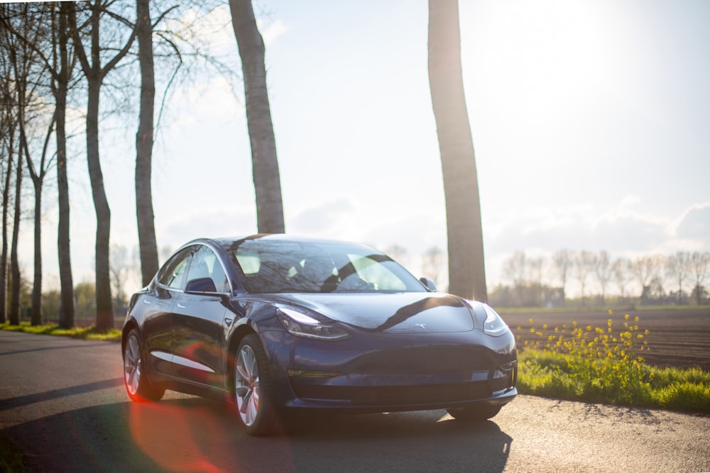 parked blue coupe beside trees during daytime