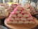 A variety of stacked sweets on wooden trays, including a prominent pyramid of pink and white coconut bars and layered nougat with nuts.
