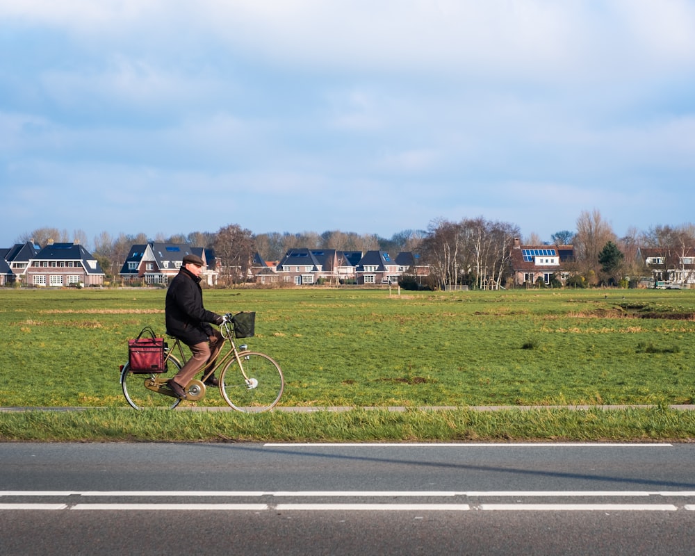 man biking near green field under blue and white skies