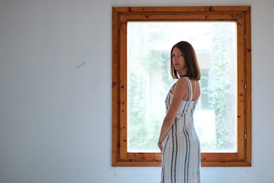 woman wearing white and blue pinstriped maxi dress i front of window appealing teams background