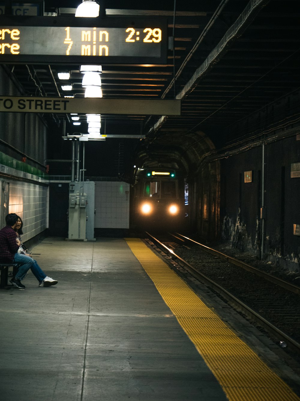 man and woman sits on bench near upcoming train