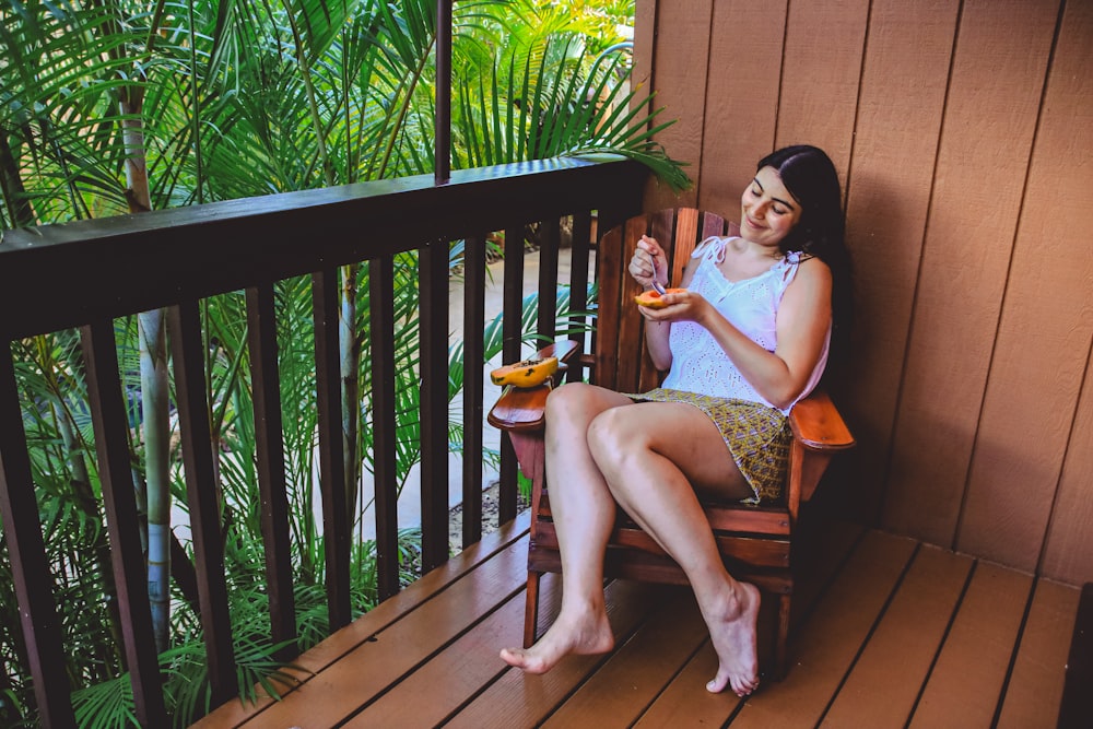 woman eating mango while sitting on armchair at the balcony of a building