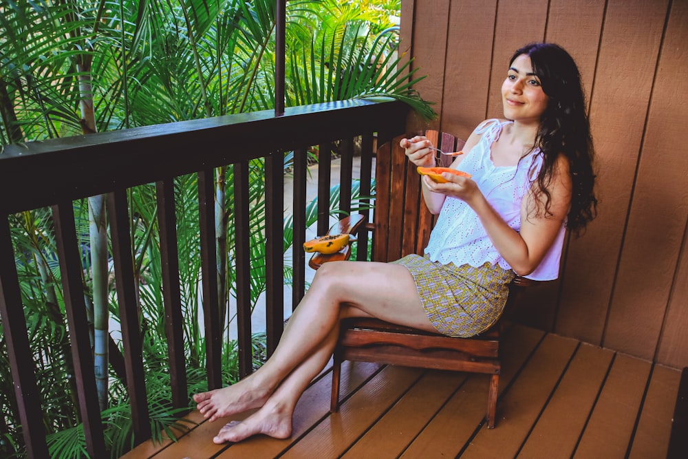 mulher comendo fruta de mamão sentada na cadeira na varanda