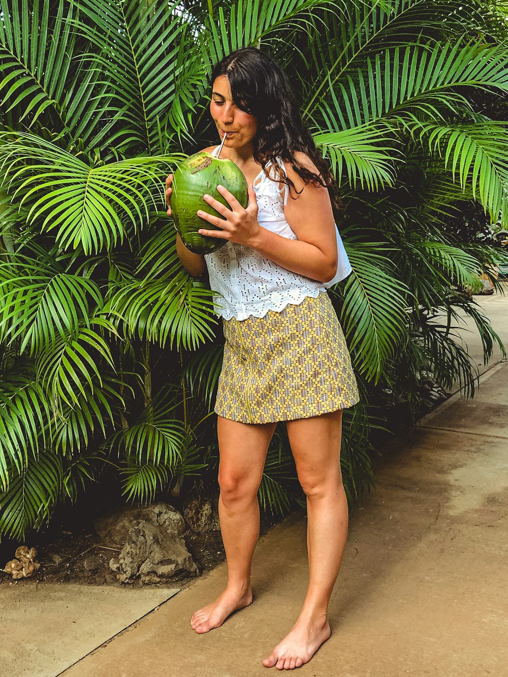 woman drinking coconut juice standing beside palm plant