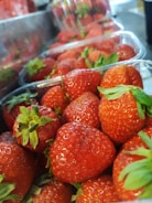 Fresh strawberries fill clear plastic containers, each fruit displaying a vibrant red hue with green leafy tops. The image gives a sense of abundance and freshness.