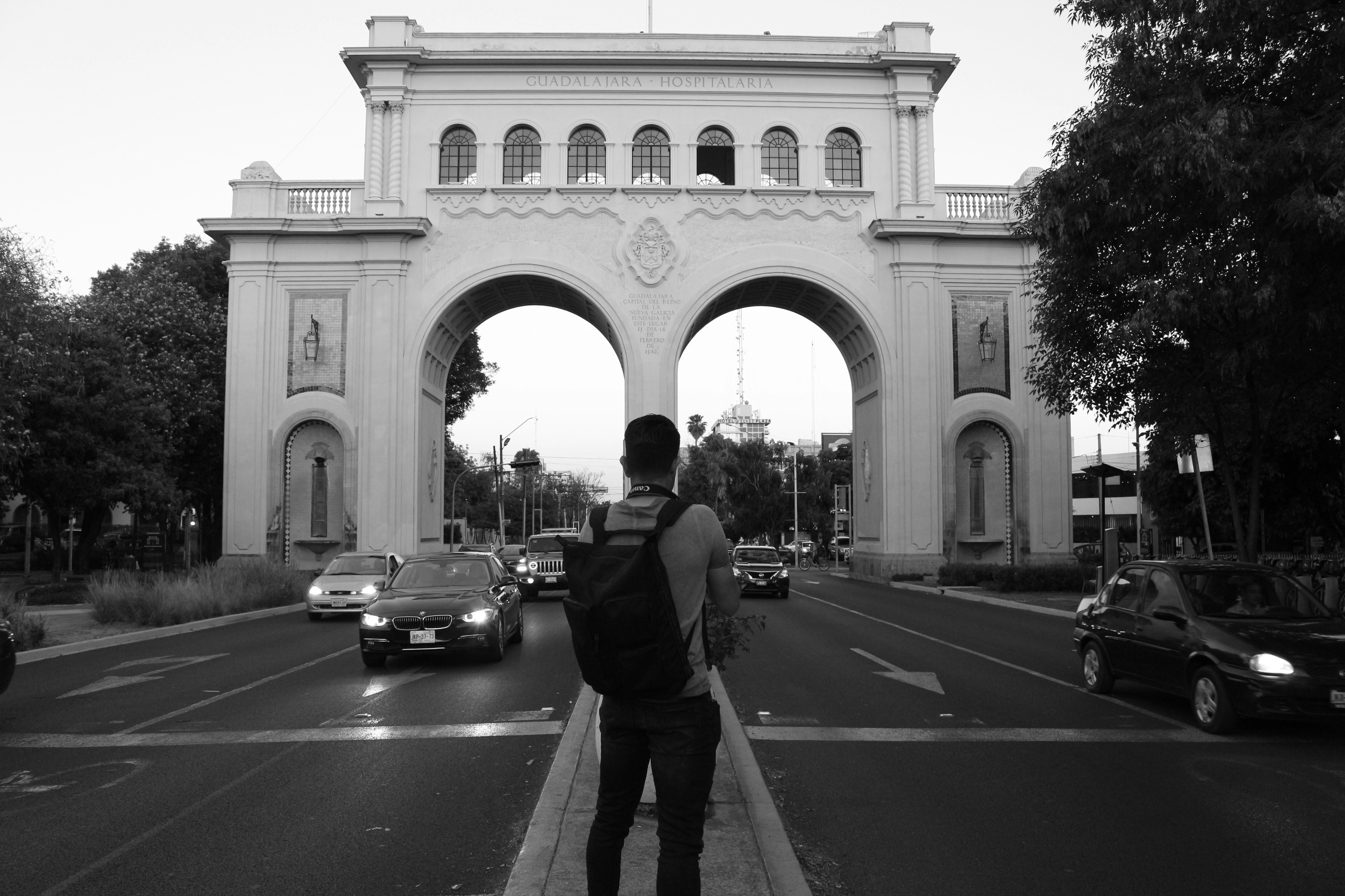 grayscale photography of man standing facing concrete structure