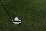 A close-up of a golf club resting on a green grass tee.