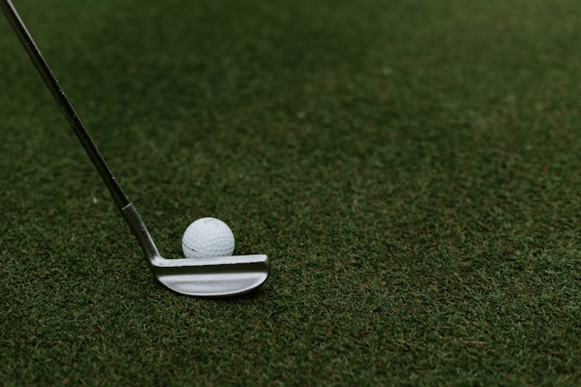 A close-up of a golf club resting on a green grass tee.