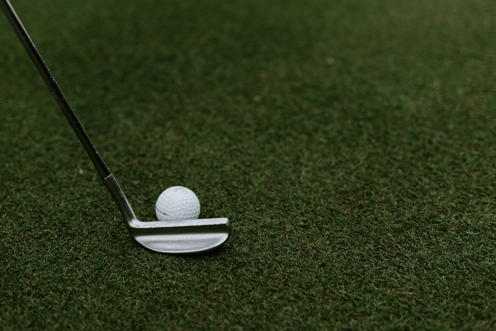 Clube de golfe preto e cinza ao lado da bola de golfe no campo de grama verde