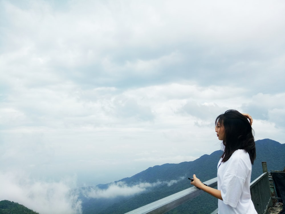 woman standing beside handrail overlooking mountain