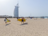 people walking and holding surfboards near Burj Al Arab building