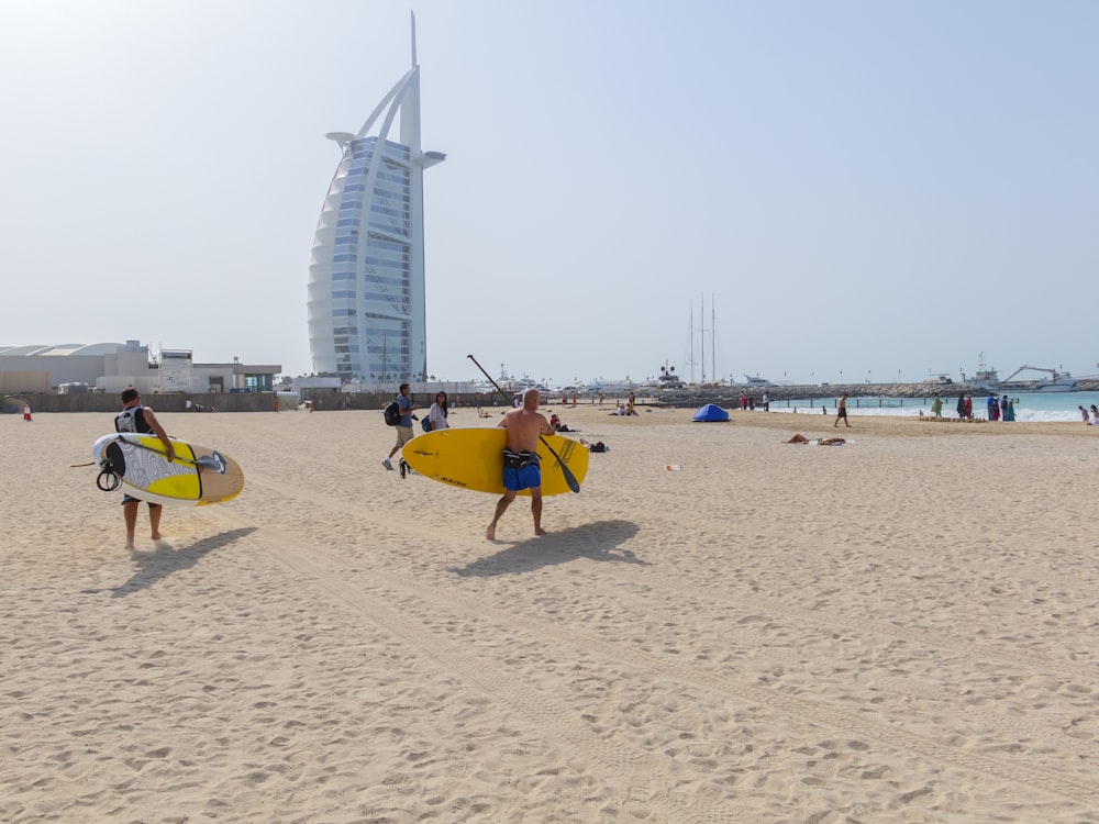 people walking and holding surfboards near Burj Al Arab building