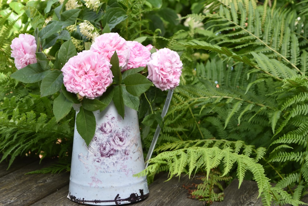 a white vase with pink flowers on a wooden table