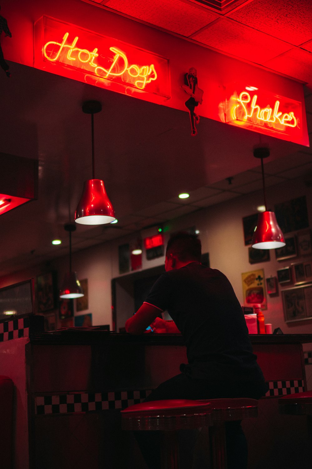man sitting under hot dogs and shakes signages