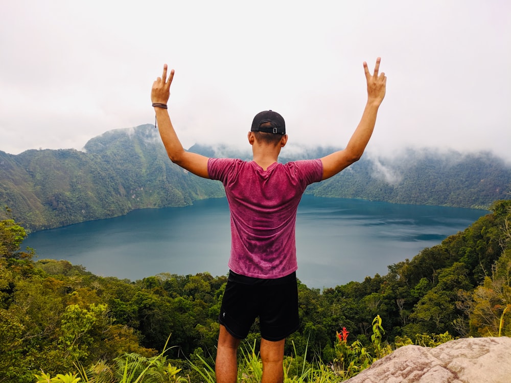 man in red shirt standing on cliff facing crater