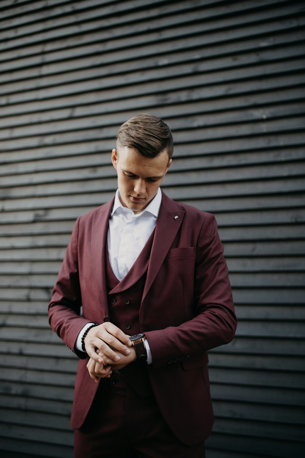 man in maroon suit looking at watch in wrist