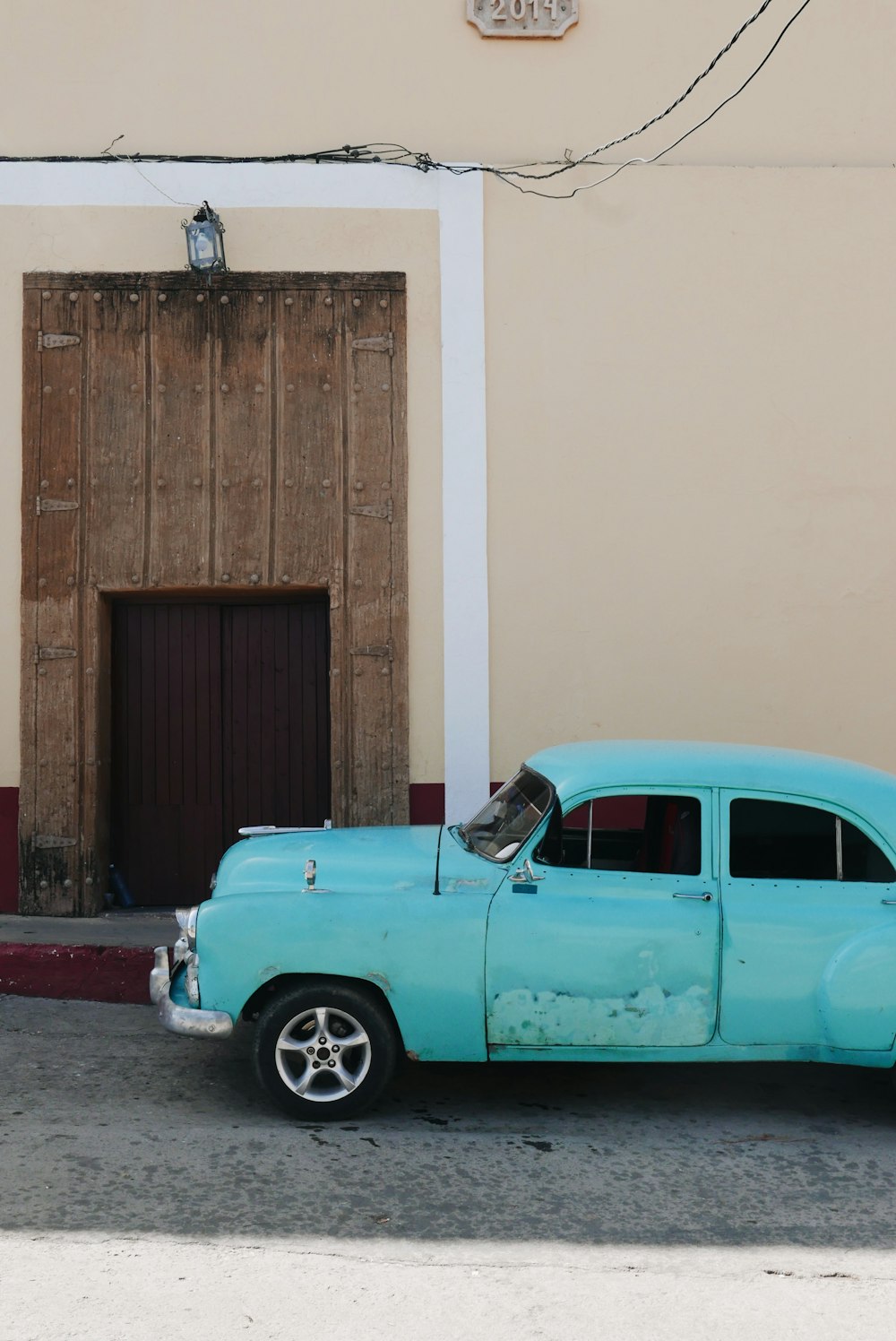 classic teal car parked beside the road near closed French doors